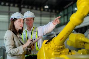 fabbrica ingegneri ispezionando su macchina con inteligente tavoletta. lavoratore lavori a pesante macchina robot braccio. il saldatura macchina con un' a distanza sistema nel un industriale fabbrica. artificiale intelligenza concetto. foto