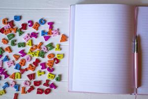 un' bloc notes con penna, rosa cactus, spiegazzato foglio di carta e multicolore lettere su un' bianca di legno desktop. foto
