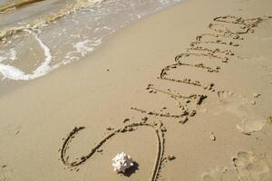il parola estate è scritto su il sabbia di mano. foto