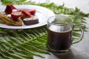 cialde con fragola, un' tazza di caffè e verde le foglie di felce su un' tavolo. bellissimo e gustoso prima colazione. foto