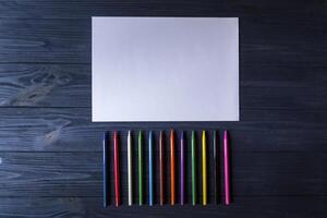 tavolozza di multicolore matite e il foglio di bianca carta su buio blu di legno scrivania. foto