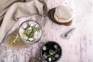 Gin Tonico con ghiaccio e rosmarino nel un' bicchiere su un' pietra su il tavolo superiore Visualizza foto