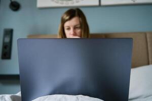 donna dire bugie nel letto e utilizzando il computer portatile foto