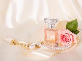 un' bellissimo composizione con un elegante profumo bottiglia, rosa Rose, un' oro collana e un' raso nastro. delicato raso beige sfondo. foto