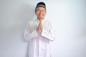 asiatico musulmano uomo indossare bicchieri e bianca stoffa sorridente fare saluto posa per Ramadhan e eid al fitr. isolato bianca sfondo foto