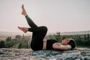 fitness donna. bene guardare mezzo anziano donna con lungo capelli, fitness istruttore nel ghette e cime fare allungamento e pilates su il roccia vicino foresta. femmina fitness yoga routine concetto. foto