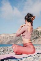 mezzo anziano bene guardare donna con nero capelli, fitness istruttore nel ghette e cime fare allungamento e pilates su yoga stuoia vicino il mare. femmina fitness yoga routine concetto. salutare stile di vita foto