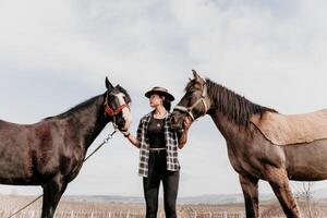 giovane contento donna nel cappello con sua cavallo nel sera tramonto luce. all'aperto fotografia con moda modello ragazza. stile di vita umore. concetto di all'aperto cavalcare, gli sport e ricreazione. foto