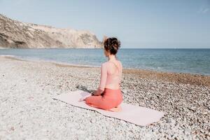 donna mare pilates. sportivo contento mezzo anziano donna praticante fitness su spiaggia vicino mare, sorridente attivo femmina formazione con squillare su yoga stuoia fuori, godendo salutare stile di vita, armonia e meditazione foto