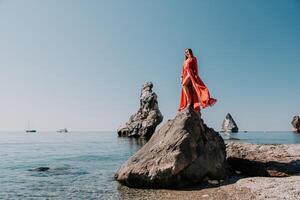 donna viaggio mare. giovane contento donna nel un' lungo rosso vestito in posa su un' spiaggia vicino il mare su sfondo di vulcanico rocce, piace nel Islanda, condivisione viaggio avventura viaggio foto