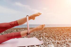 donna mare pilates. sportivo contento mezzo anziano donna praticante fitness su spiaggia vicino mare, sorridente attivo femmina formazione con squillare su yoga stuoia fuori, godendo salutare stile di vita, armonia e meditazione foto