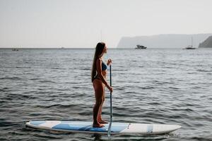 donna mare sup. vicino su ritratto di contento giovane caucasico donna con lungo capelli guardare a telecamera e sorridente. carino donna ritratto nel un' blu bikini in posa su cenare tavola nel il mare foto