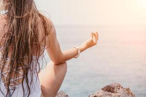 vicino su yoga mano gesto di donna fare un all'aperto meditazione. sfocato mare sfondo. donna su yoga stuoia nel spiaggia meditazione, mentale Salute formazione o mente benessere di oceano, mare foto