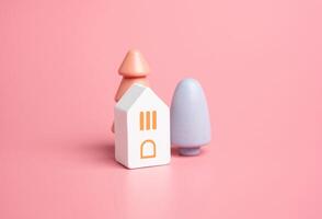 Casa e colorato alberi su un' rosa sfondo. di legno figurine giocattoli. acquistare un' Casa. bene alloggi. mutuo. accogliente e dolce toni. pastello rosa colori. foto
