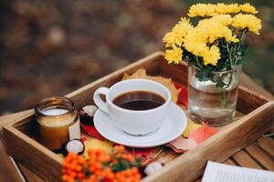 un' tazza di tè o caffè su un' di legno vassoio contro il autunno sfondo con caduto foglie, candela e fiori, autunno umore foto