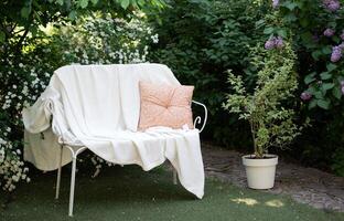 forgiato bianca metallo panchina nel il giardino con un' coperta e un' cuscino foto