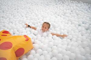 contento poco ragazza giocando bianca plastica palle piscina nel divertimento parco. terreno di gioco per bambini. foto