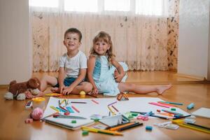 bambini disegno su pavimento su carta. prescolastico ragazzo e ragazza giocare su pavimento con educativo giocattoli - blocchi, treno, Ferrovia, aereo. giocattoli per prescolastico e asilo. bambini a casa o asilo nido foto