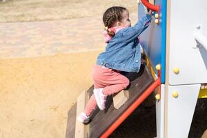 carino poco caucasico ragazza su il terreno di gioco, contento bambino con piacere la spesa tempo all'aperto, contento spensierato infanzia foto