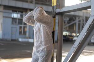 disperazione assistenza sanitaria lavoratore nel bianca covid protettivo tuta da lavoro. stanco maschio caucasico medico afferra il suo testa rannicchiarsi nel depressione durante coronavirus pandemia foto