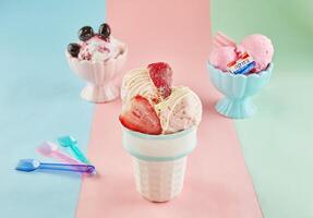 tre ghiaccio crema sapori nel bianca e rosa tazze con cucchiai su un' blu, rosa, e verde sfondo. foto