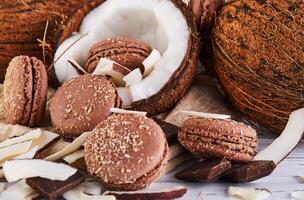 Noce di cocco macarons con cioccolato e Noce di cocco fiocchi su un' tavolo con un' Noce di cocco nel il sfondo foto