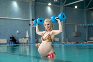 incinta donna in piedi nel acqua con manubri in casa nuoto piscina foto