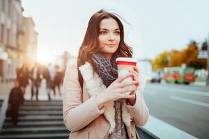 bella giovane donna nel elegante cappotto Tenere tazza nel mani. caldo morbido accogliente Immagine. particolari. potabile prendere lontano caffè. prima colazione su il andare. instagram stile tonica Immagine foto