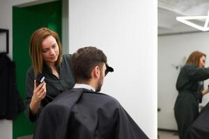 bello blu con gli occhi uomo seduta nel barbiere negozio. parrucchiere parrucchiere donna taglio il suo capelli. femmina barbiere. foto