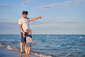 giovane caucasico papà con poco figlio camminare caldo estate giorno lungo il mare costa. estate famiglia vacanza concetto. amicizia padre e figlio. foto