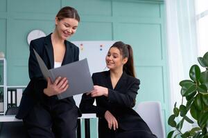 giovane donne capi siamo controllo finanziario dichiarazioni a partire dal carta documenti. Due femmina fiducioso attività commerciale lavoratore vestito nero completo da uomo nel ufficio controllo finanziario documento foto