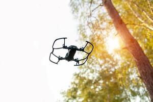 piccolo inteligente fuco Quadrocopter volante su bianca cielo e verde alberi. foto