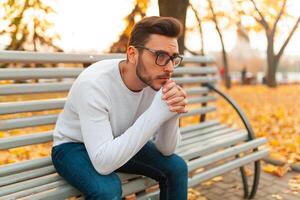 un' solitario bello uomo si siede triste nel il parco su un' panca. autunno stagione, giallo le foglie su sfondo. solitudine concetto. il alunno fatto non passaggio il esami o rotto su con il ragazza foto