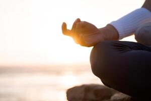 donna pratica yoga loto posa per meditazione con estate vacanza roccioso spiaggia felicità e rilassamento. calma femmina esercizio con yoga meditare oceano spiaggia con tramonto d'oro volta. foto