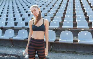 bellissimo caucasico ragazza atleta detiene nel sua mani un' acqua nel un' plastica bottiglia foto