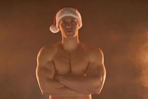 ritratto di muscolare uomo indossare Natale Santa cappello, piegato mani su fumoso sfondo foto