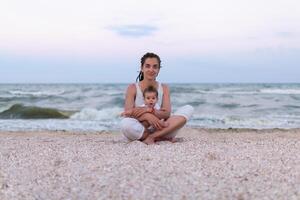 contento famiglia madre e bambino figlia fare yoga, meditare nel loto posizione su spiaggia a tramonto foto