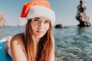 donna mare sup. vicino su ritratto di contento giovane caucasico donna con lungo capelli nel Santa cappello guardare a telecamera e sorridente. carino donna ritratto nel un' bianca bikini in posa su cenare tavola nel il mare foto