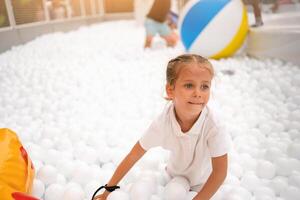 contento poco ragazza giocando bianca plastica palle piscina nel divertimento parco. terreno di gioco per bambini. foto