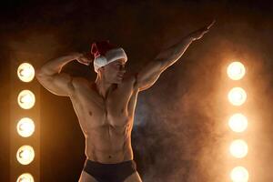 muscolare atleta nel Santa cappello in posa su illuminato sfondo, mostrando il suo muscoli, atletico competitivo posa foto