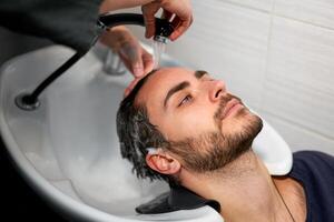 donna l'applicazione shampoo massaggio capelli cliente uomo lavare capelli nel bellezza salone parrucchiere lavaggio capelli. contento caucasico tipo godere servizio nel barbiere foto