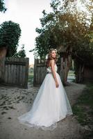 un' carino Riccio donna nel un' bianca nozze vestito con un' nozze mazzo e ghirlanda nel sua capelli in piedi indietro per il telecamera nel natura. concetto sfuggito sposa. inoltrare per un' contento luminosa futuro scappa foto