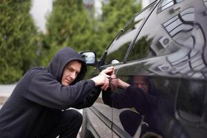 auto jacking ladro rubare auto rottura porta penale lavoro scassinatore dirottamenti auto ladro nero Balaclava felpa con cappuccio provando rompere in veicolo Cacciavite strada crimine violenza gangster rapinatore automobile foto