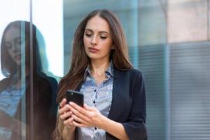 attività commerciale donna 35 anni vestito banda camicia e nero giacca con lungo capelli in piedi vicino ufficio edificio all'aperto uso smartphone foto