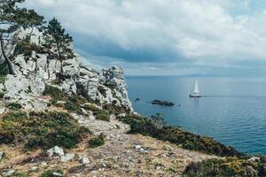 panoramico Visualizza di Pacifico oceano blu trasparente acqua, un' bianca sport moderno lusso yacht vela barca galleggiante e un' verde riva con foresta, colline. vacanza di il acqua e vela gara. foto