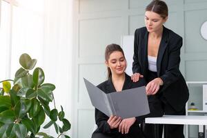 giovane donne capi siamo controllo finanziario dichiarazioni a partire dal carta documenti. Due femmina fiducioso attività commerciale lavoratore vestito nero completo da uomo nel ufficio controllo finanziario documento foto