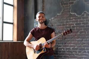 uomo con acustico chitarra contro mattone parete giocando musica cantando canzoni godere vita medio sparare foto