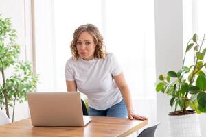 attività commerciale donna utilizzando il computer portatile in piedi vicino scrivania bianca ufficio interno con pianta della casa guardare a telecamera foto