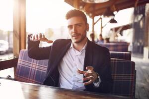 bello giovane uomo d'affari seduta nel un' estate all'aperto bar su il sfondo di il sera tramonto a il negoziazione tavolo foto