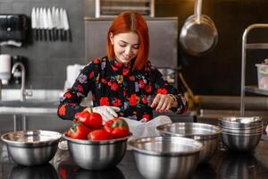 bellissimo giovane dai capelli rossi ragazza nel sera vestito è preparazione cibo nel un' professionale cucina. foto